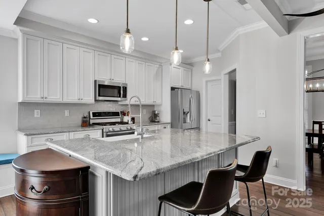 a kitchen with stainless steel appliances granite countertop a stove a refrigerator a sink a dining table and chairs with wooden floor