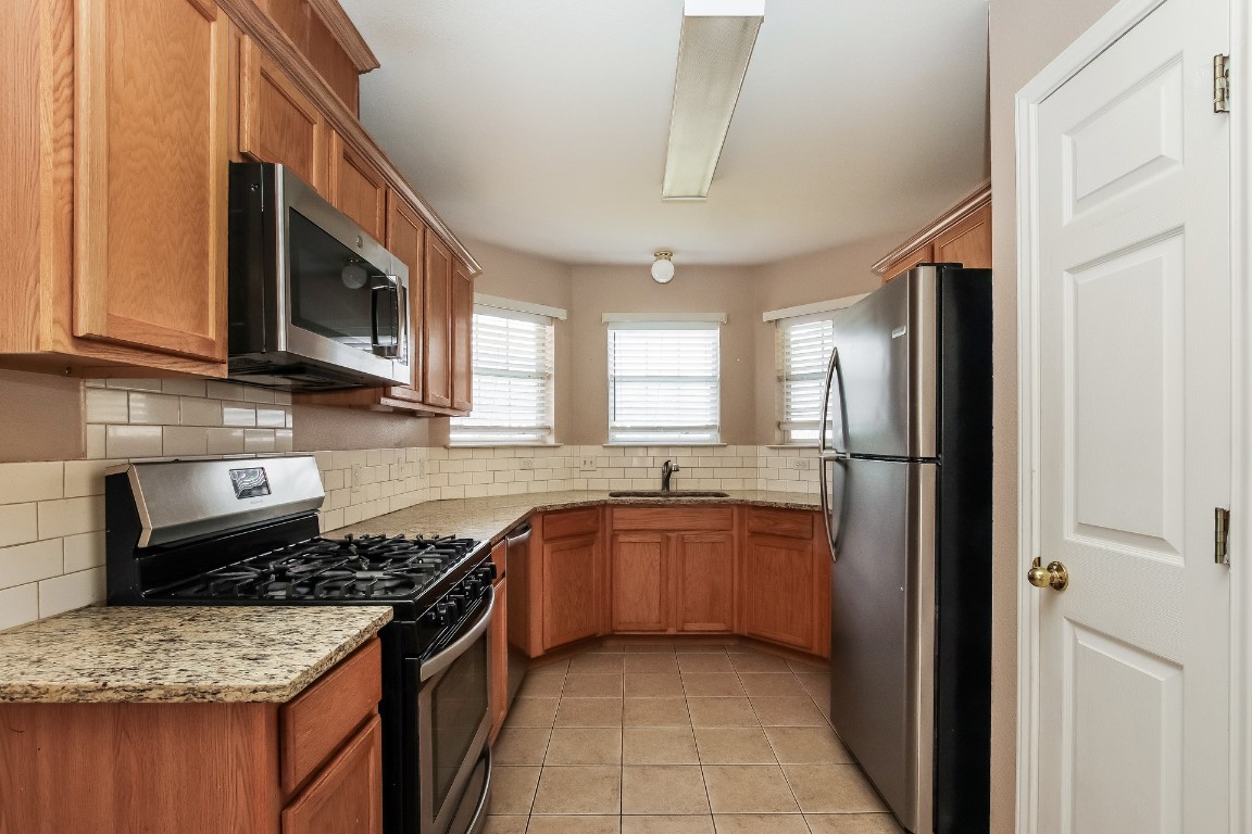 21304 Secretariat Ridge Lane Pflugerville, TX 78660 - Photo 10 of 29 a kitchen with stainless steel appliances granite countertop a stove top oven a sink dishwasher and a refrigerator with wooden cabinets