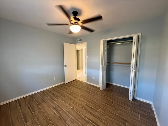 a view of an empty room with wooden floor and a ceiling fan