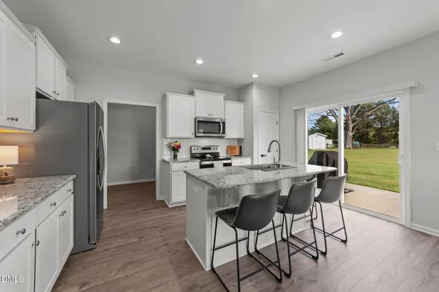 a kitchen with kitchen island granite countertop a stove a sink a refrigerator and a dining table with wooden floor