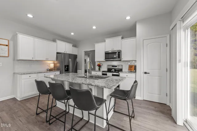 a kitchen with stainless steel appliances granite countertop a stove a sink a microwave a refrigerator and white cabinets with wooden floor