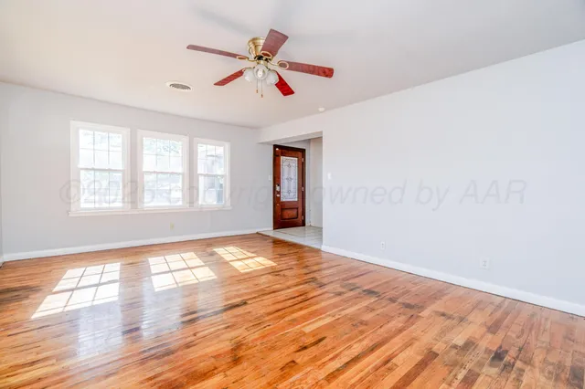 a view of an empty room with wooden floor and a window