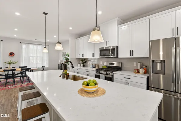 a kitchen with stainless steel appliances a refrigerator a stove a sink dishwasher a dining table and chairs with wooden floor