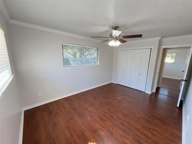 an empty room with wooden floor chandelier fan and windows