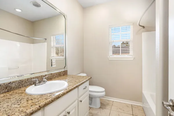 a bathroom with a granite countertop sink a mirror a toilet and a window