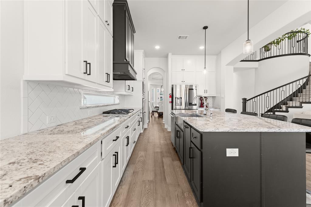 600 St Andrew Lane Prosper, TX 75078 - Photo 7 of 29 Kitchen featuring two tone cabinetry, light wood-style flooring, arched walkways, light stone counters, and a kitchen island with sink