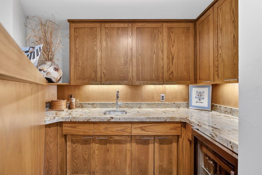 1080 North Greenbrier Road Nocona, TX 76255 - Photo 15 of 40 Custom Wet bar area with cabinetry with brushed nickel hardware, light granite countertops, stainless steel sink with gooseneck faucet, and integrated under-cabinet lighting