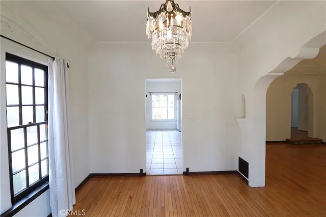 an empty room with wooden floor chandelier and windows