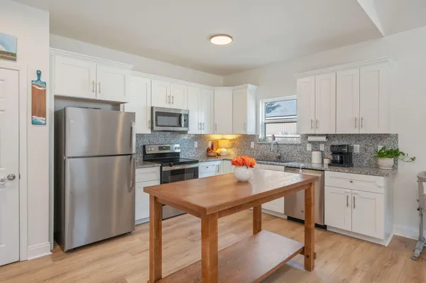 a kitchen with a refrigerator a stove a sink and white cabinets with wooden floor