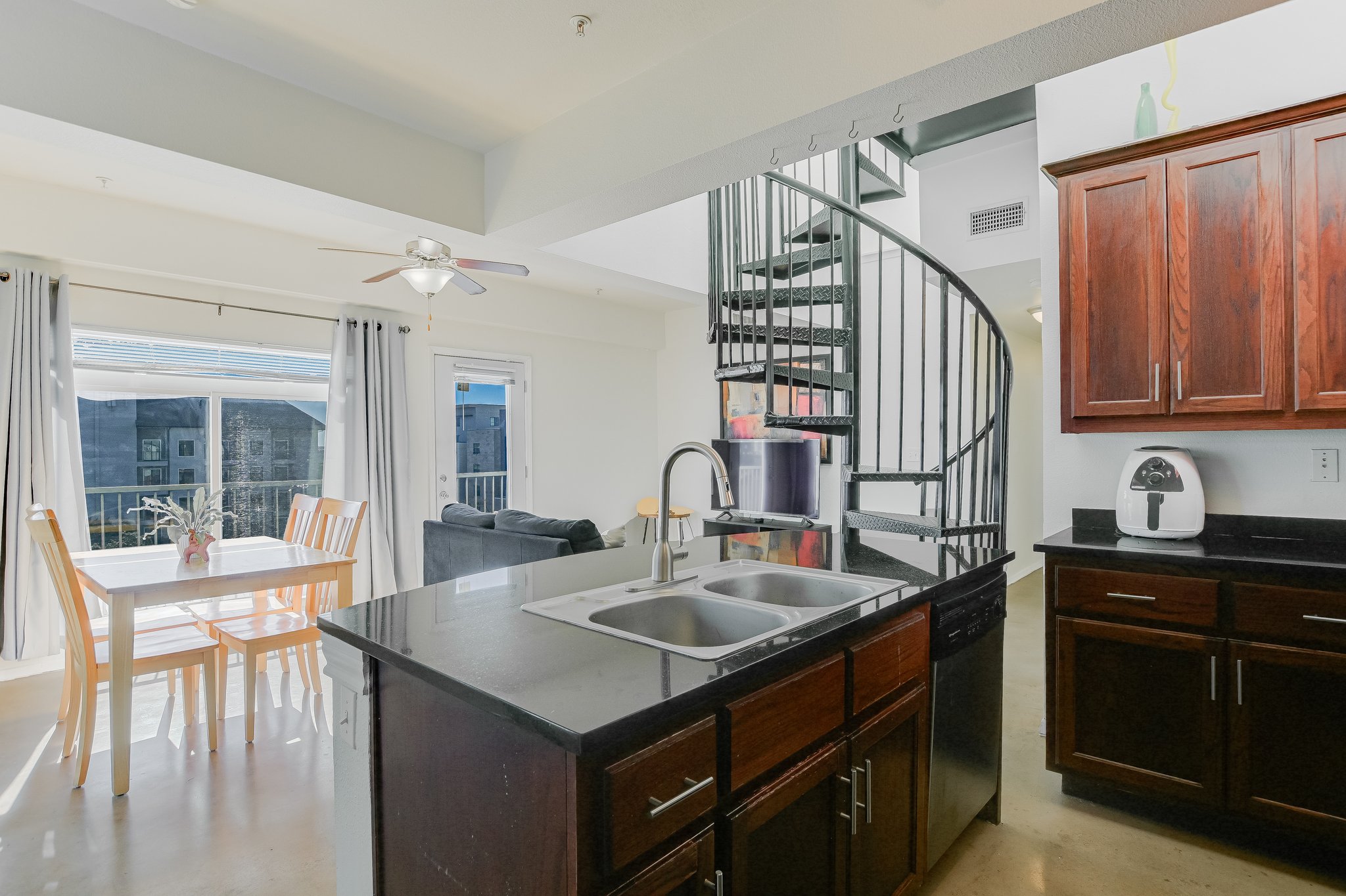 910 West 25th Street, Unit 607 Austin, TX 78705 - Photo 12 of 19 Kitchen featuring finished concrete flooring, a ceiling fan, a center island with sink, stainless steel dishwasher, and dark brown cabinetry