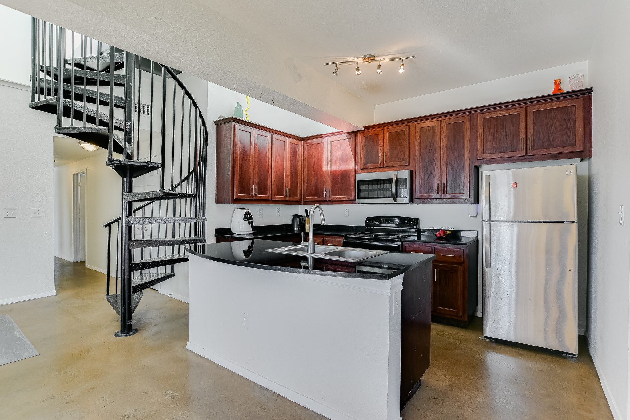 910 West 25th Street, Unit 607 Austin, TX 78705 - Photo 13 of 19 Kitchen featuring appliances with stainless steel finishes, concrete flooring, dark stone counters, and a peninsula