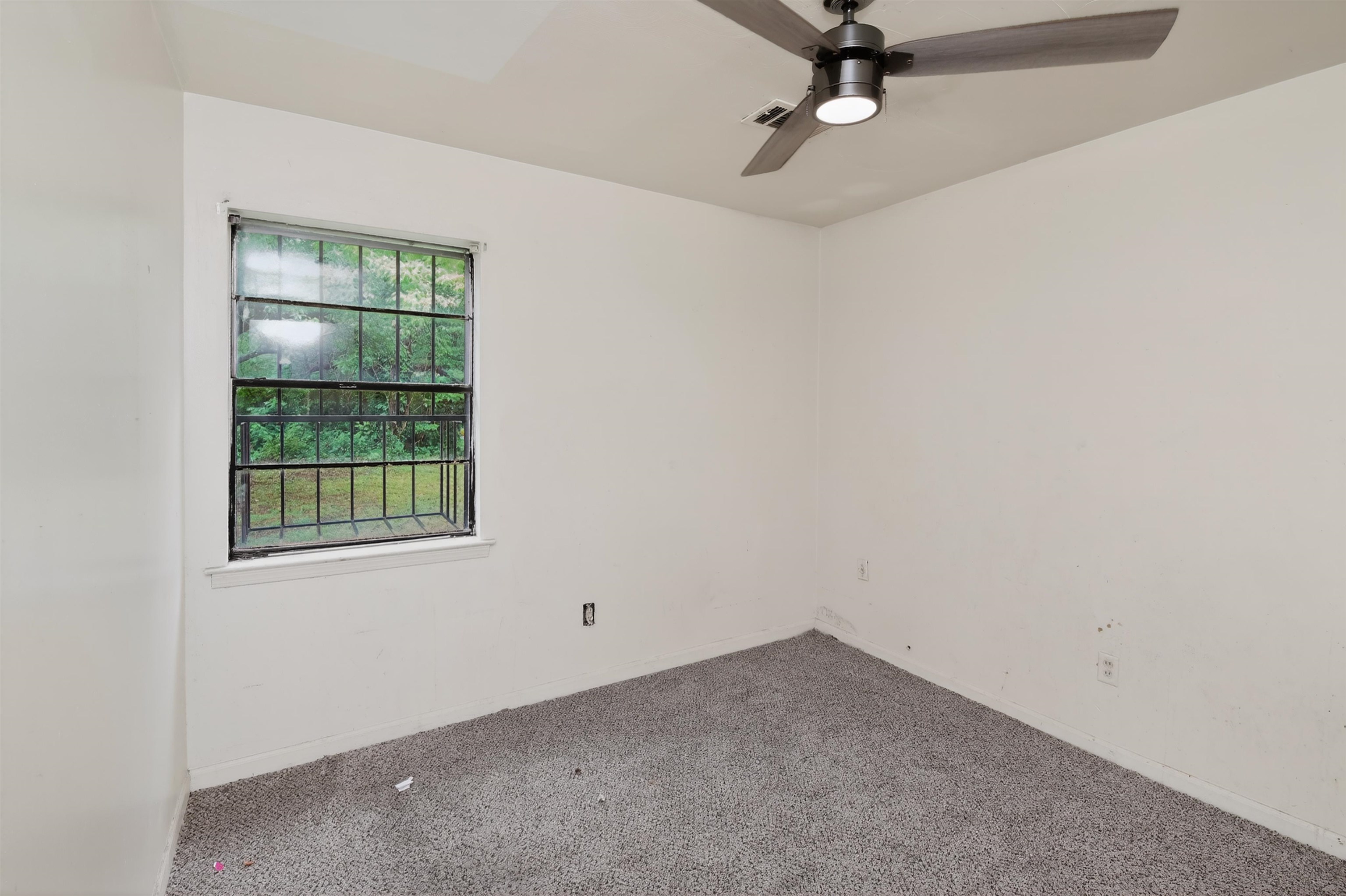 3451 Birdsong Ferry Road Memphis, TN 38118 - Photo 16 of 27 Room featuring a window with security bars, a ceiling fan with integrated lighting, and gray carpeted flooring