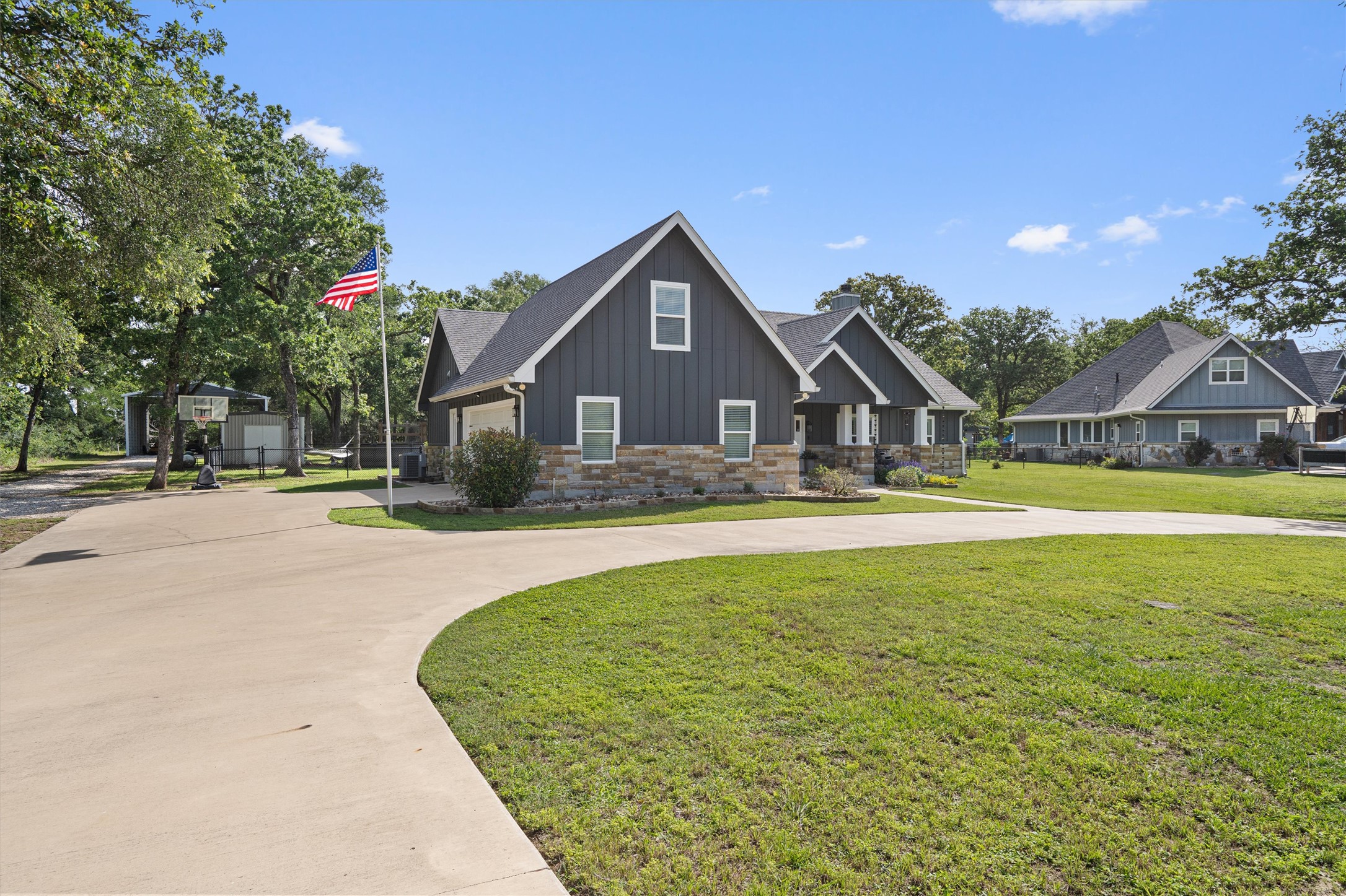 136 Fawn Hollow Elgin, TX 78621 - Photo 2 of 40 Contemporary home featuring dark vertical siding, stone accents, a multi-gabled roofline, and a concrete driveway