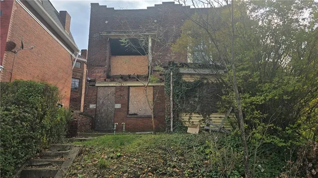 a view of a brick house with a small yard and large tree