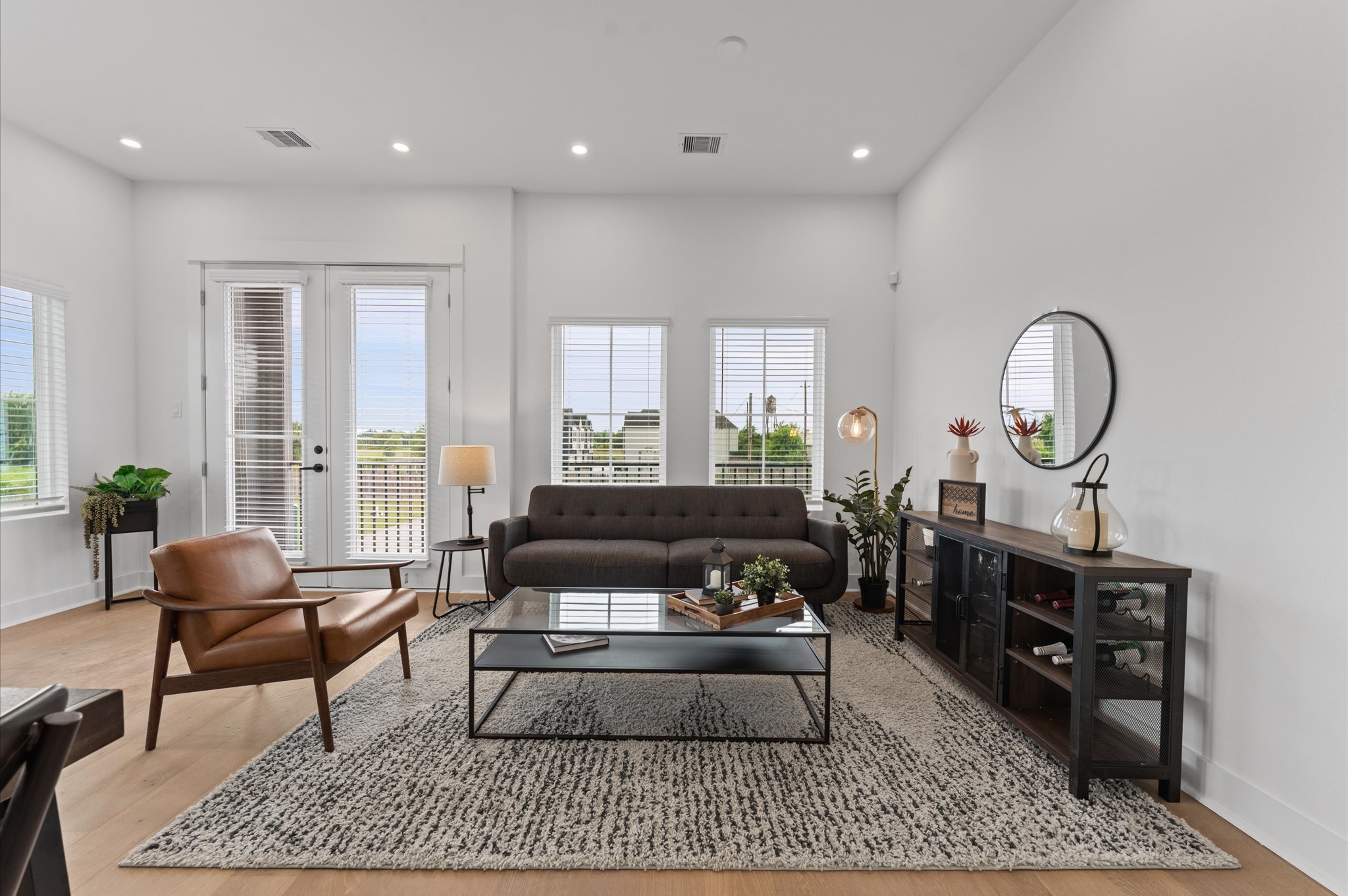 Perched on the second floor, this open-concept living, dining, and kitchen area flows effortlessly beneath high ceilings and across rich engineered hardwood floors that unify the space with warmth and elegance. A set of French doors anchors the room, inviting natural light and offering a glimpse of downtown through the balcony beyond. The layout encourages seamless entertaining and everyday comfort, with each zone connected yet distinct, framed by clean lines and contemporary finishes.