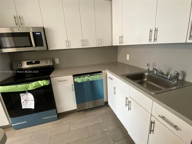 a kitchen with a sink a stove top oven a refrigerator and white cabinets