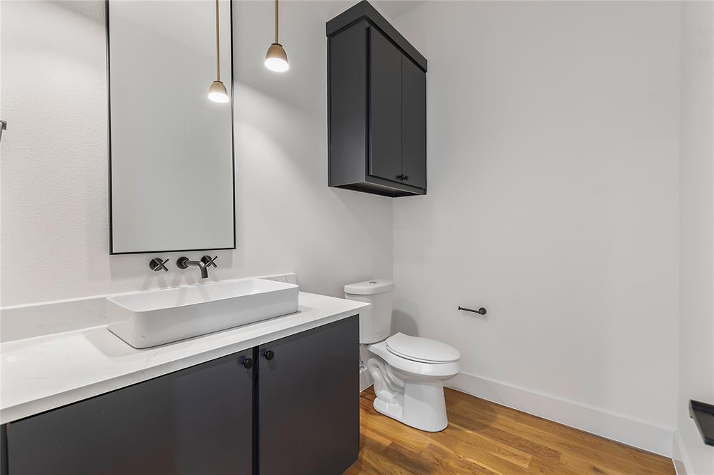 430 Whispering Way Red Oak, TX 75154 - Photo 26 of 40 Modern bathroom featuring wood-finish flooring, a rectangular vessel sink, a wall-mounted faucet, and dark cabinetry