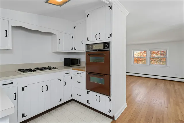 a kitchen with granite countertop a stove a microwave a sink and white cabinets with wooden floor