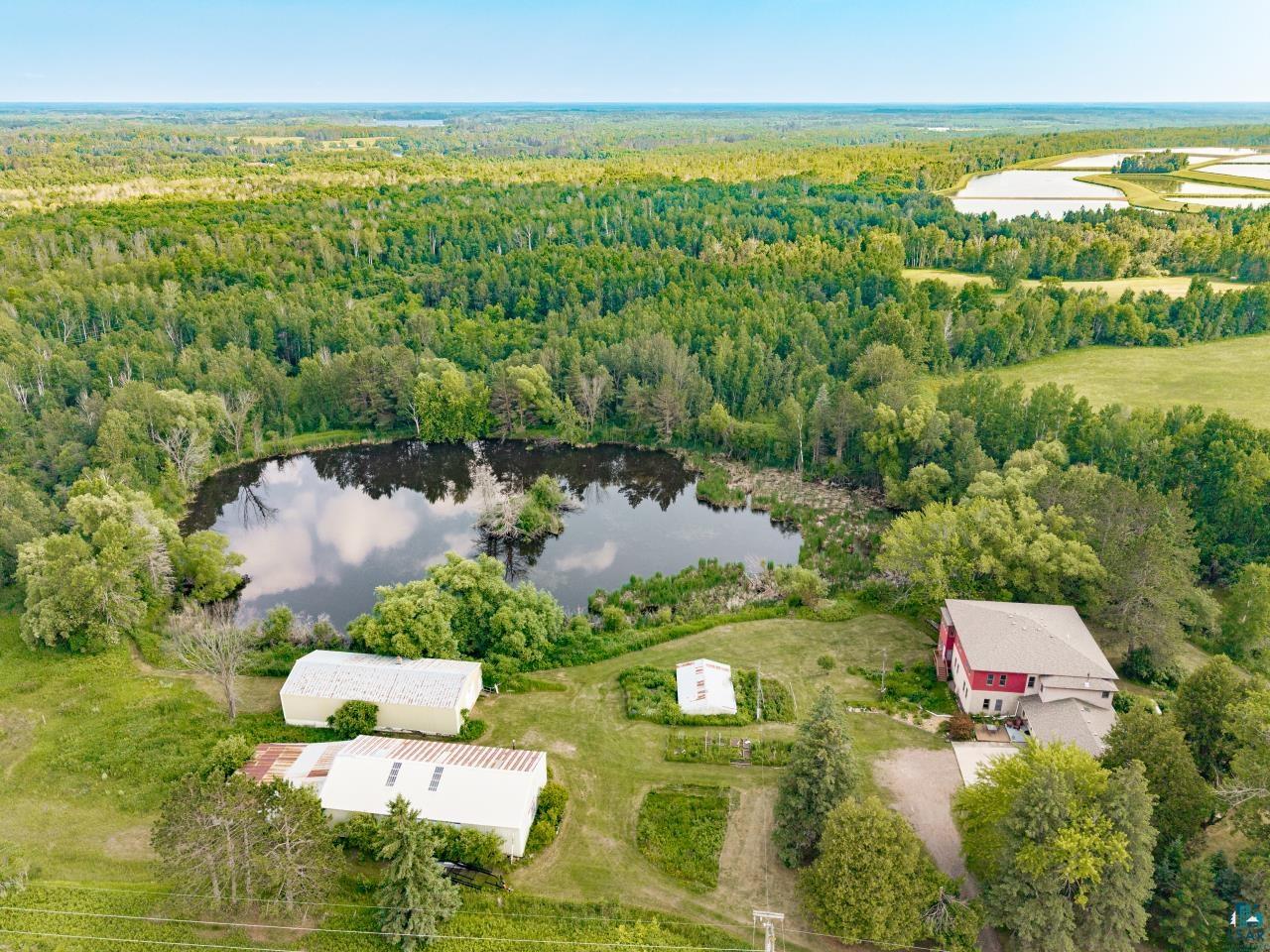 4800 Tower Road Moose Lake, MN 55767 - Photo 38 of 83 Expansive property featuring a central pond, surrounding mature trees, a red multi-story residence, two additional outbuildings, and cultivated garden beds