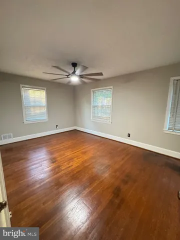 an empty room with wooden floor chandelier fan and windows