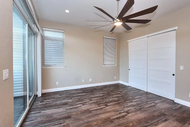 an empty room with wooden floor fan and windows