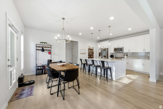 1038 South Old Towne Road Layton, UT 84041 - Photo 5 of 39 Open-concept living space featuring wood-finish flooring, a modern white kitchen with an island and stainless steel appliances, recessed lighting, and a dining area illuminated by a contemporary chandelier