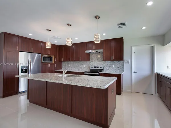 a large kitchen with stainless steel appliances kitchen island granite countertop a refrigerator and a sink
