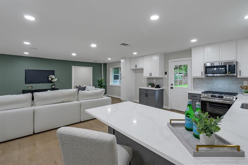 4815 Kelman Street Dallas, TX 75214 - Photo 19 of 37 Open-concept living area featuring recessed lighting, light wood-finish flooring, and a kitchen with white cabinetry, stainless steel appliances, and a solid surface island