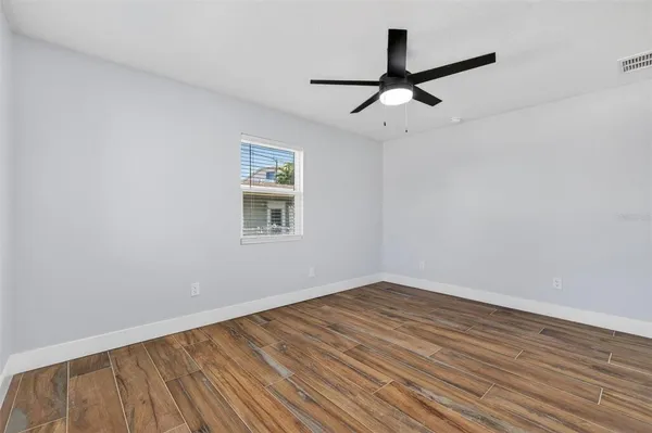 an empty room with wooden floor ceiling fan and windows