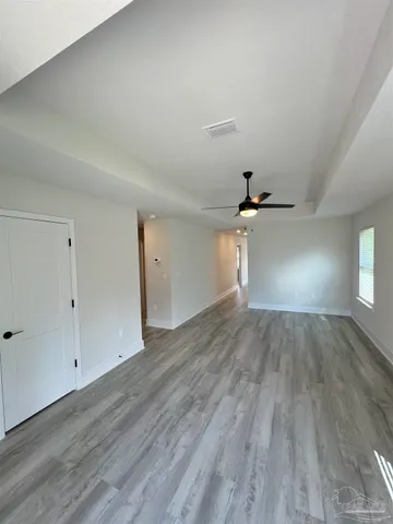 an empty room with wooden floor chandelier fan and windows