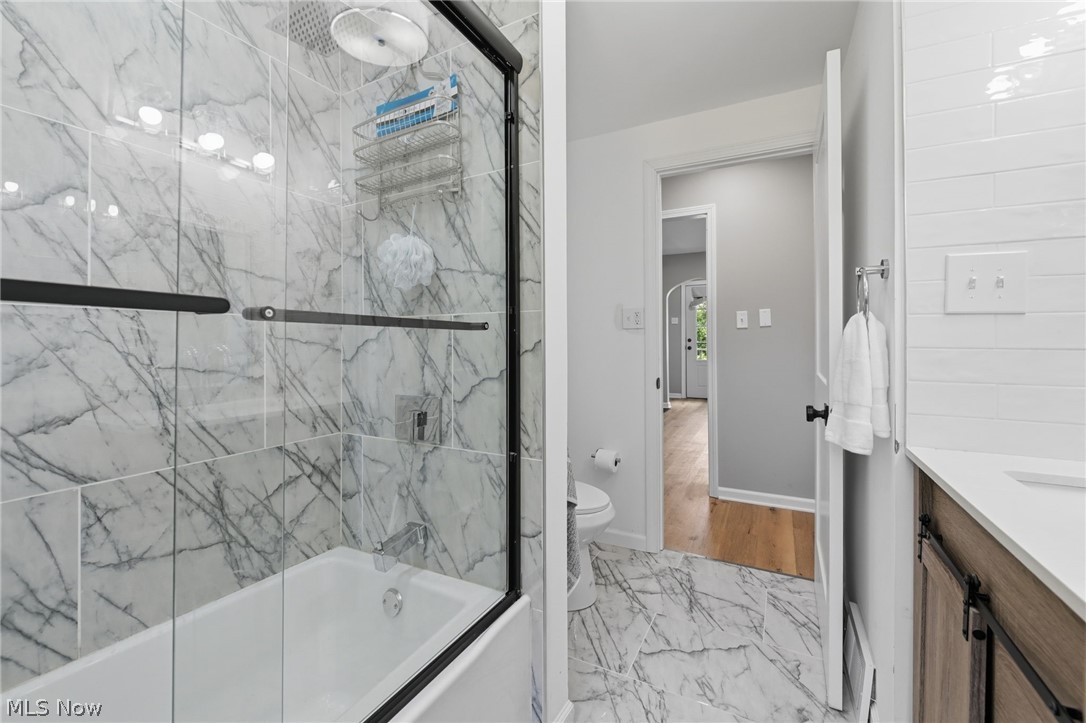 951 Bey Road Akron, OH 44312 - Photo 16 of 34 First floor bathroom featuring a tiled tub-shower combination with sliding glass doors, a vanity with a white countertop and wood-finish cabinetry, and a toilet