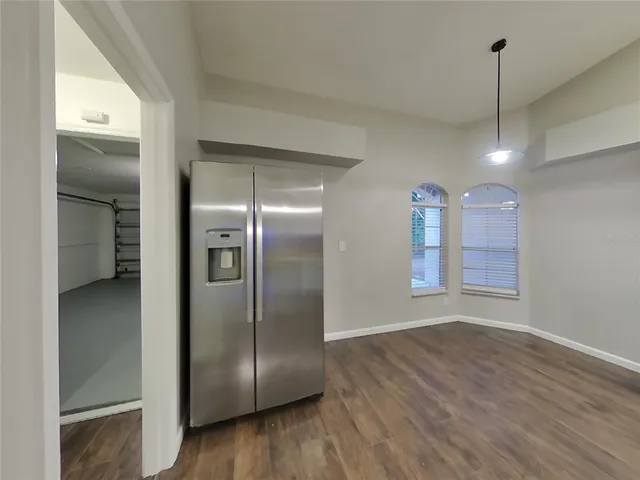 a view of a refrigerator in kitchen and an empty room with wooden floor