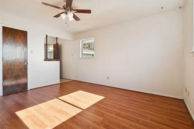 an empty room with wooden floor chandelier fan and windows