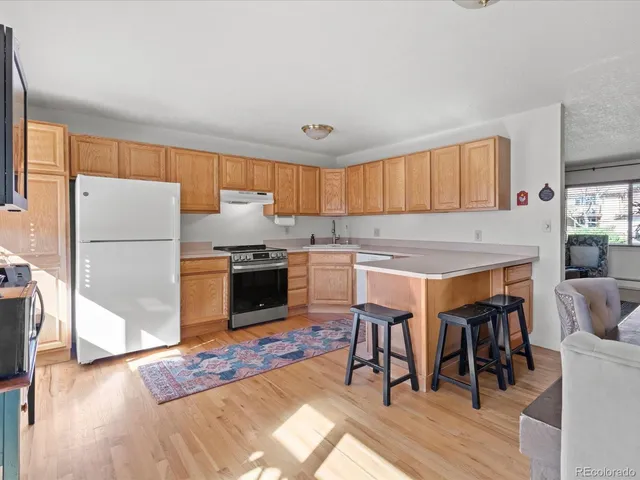 a kitchen with stainless steel appliances granite countertop a refrigerator a stove a sink a dining table and chairs with wooden floor