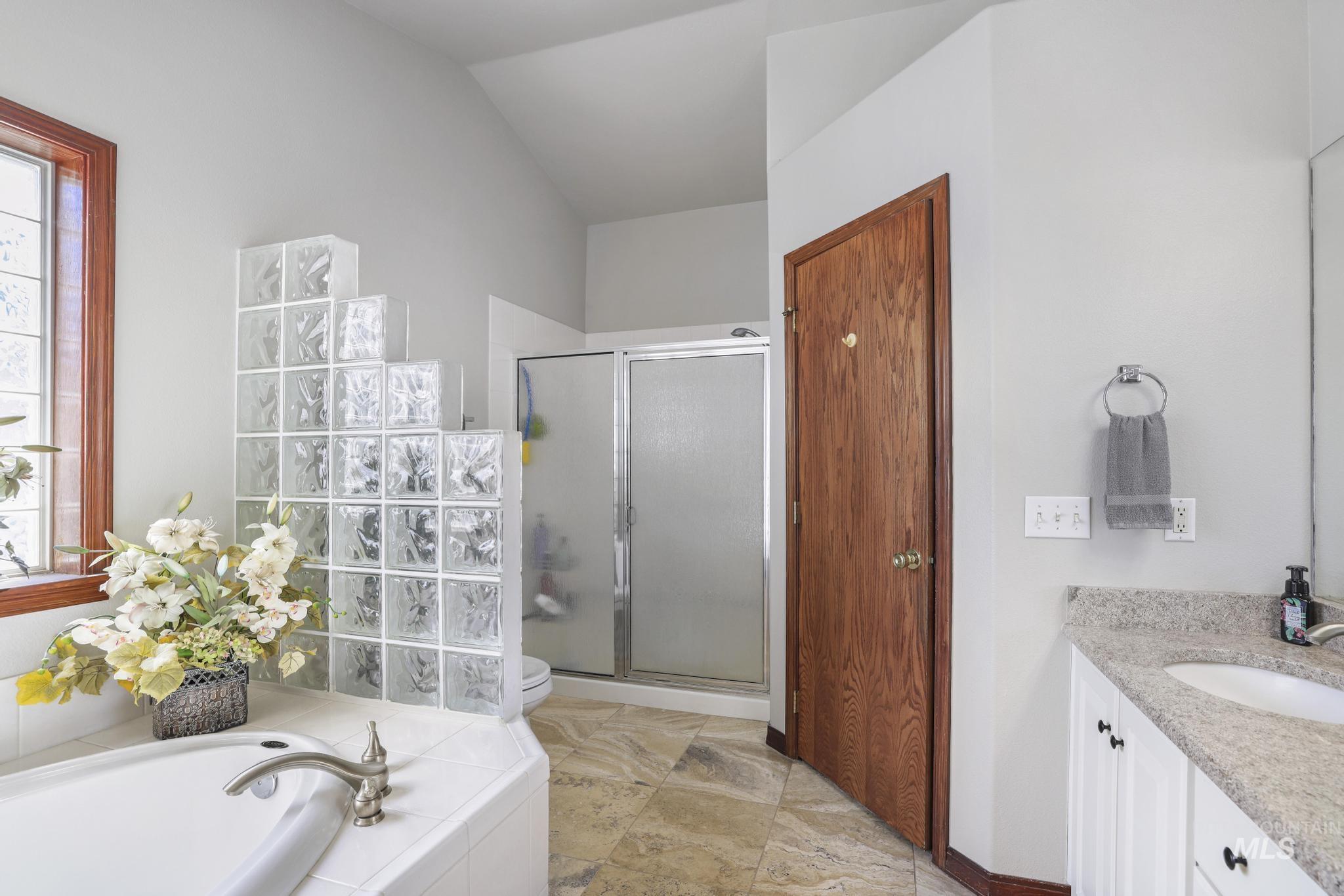 1558 Brookside Loop Twin Falls, ID 83301 - Photo 22 of 47 Bathroom featuring a tiled soaking tub with a brushed nickel faucet, a glass block partition, a shower with a sliding glass door, a vanity with a light-colored countertop and white cabinetry, and wood-finish flooring