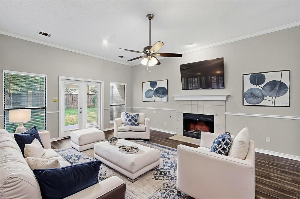 820 Charter Oak Street Allen, TX 75002 - Photo 8 of 37 Living room with crown molding, a tiled fireplace, wood finished floors, ceiling fan, and french doors