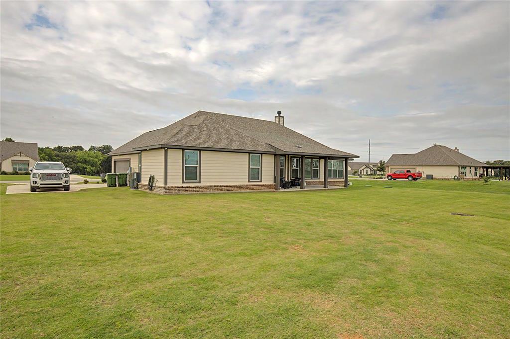 185 Chester Road Springtown, TX 76082 - Photo 36 of 40 Expansive green lawn surrounds the property, featuring a covered patio with dark posts, multiple windows, and a side-entry garage