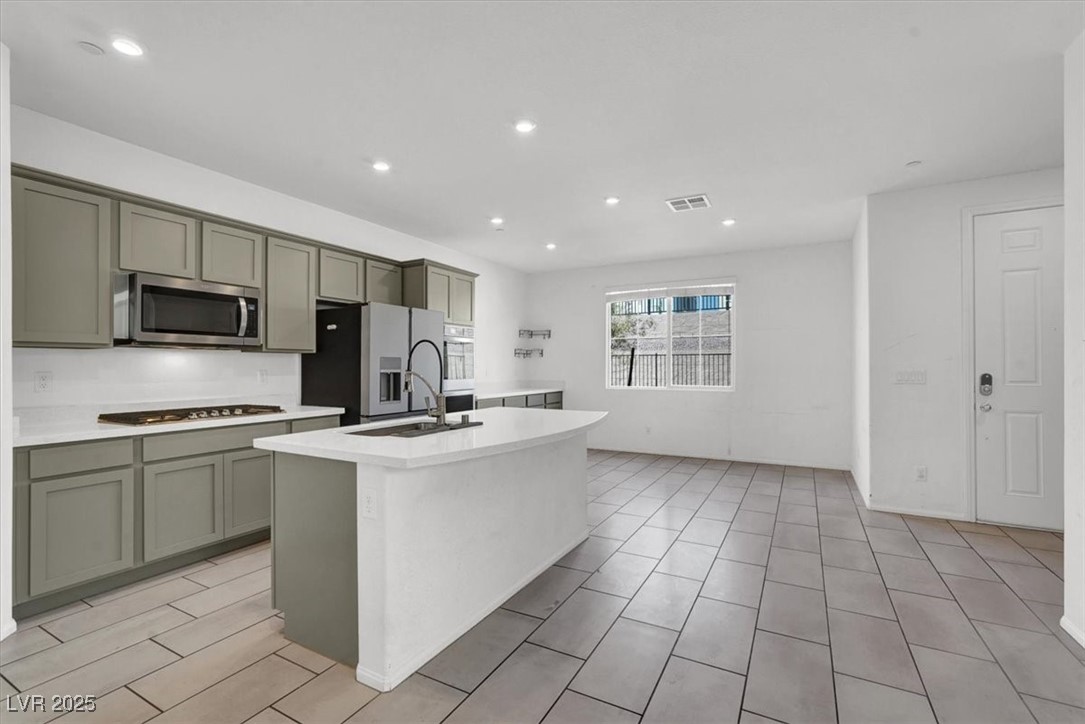 8033 Skye Foxx Street Las Vegas, NV 89166 - Photo 3 of 25 Kitchen featuring an island with sink, appliances with stainless steel finishes, recessed lighting, gray cabinets, and light stone countertops