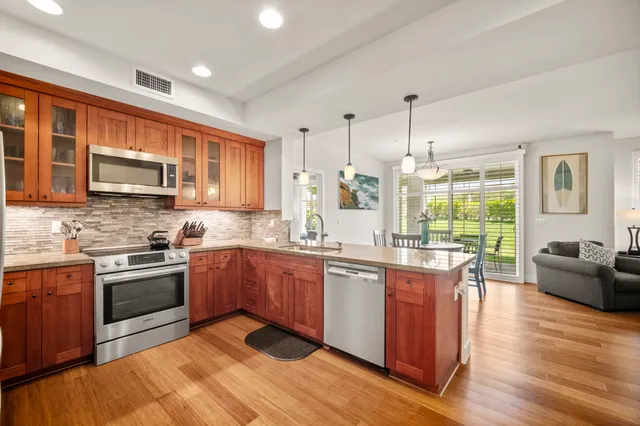 a kitchen with stainless steel appliances granite countertop wooden cabinets a sink dishwasher a stove and a refrigerator with wooden floor