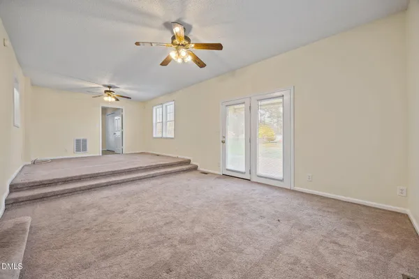 an empty room with chandelier fan and kitchen view