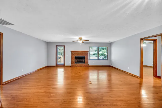 an empty room with wooden floor fireplace and windows
