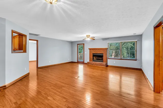 an empty room with wooden floor fireplace and windows