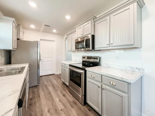 a kitchen with stainless steel appliances granite countertop a refrigerator a stove top oven a sink and dishwasher with wooden floor