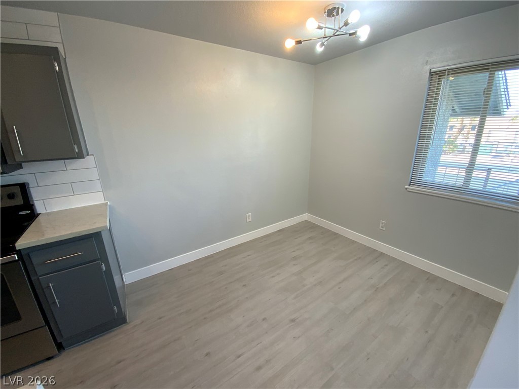 466 East Sunset Road, Unit C Henderson, NV 89011 - Photo 4 of 12 Unfurnished dining area with baseboards, light wood-style floors, and a chandelier