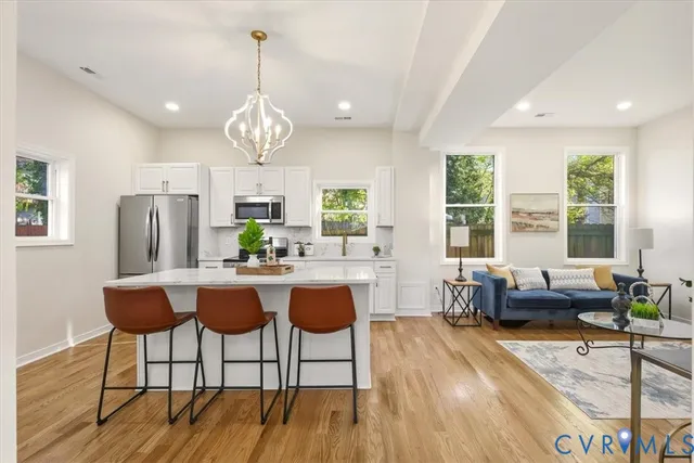 a kitchen with stainless steel appliances granite countertop a refrigerator a stove a microwave oven a sink dishwasher and white cabinets with wooden floor