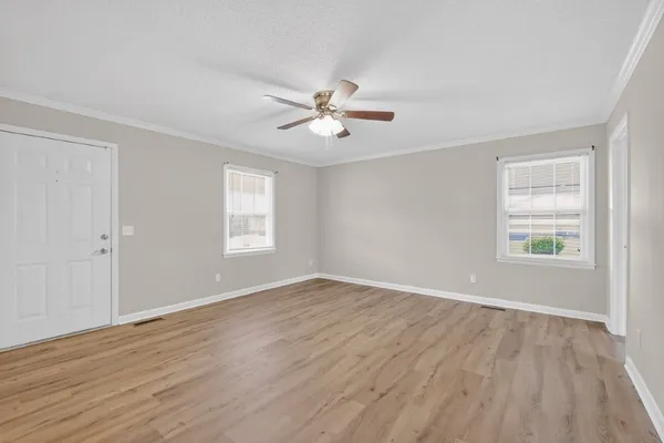 an empty room with wooden floor ceiling fan and windows