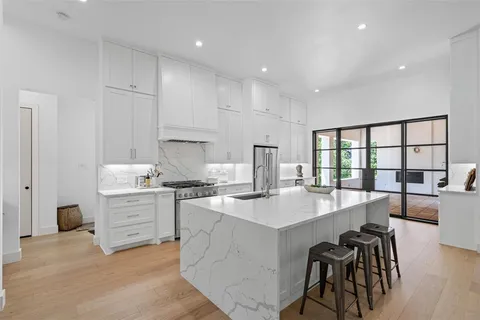 a large white kitchen with granite countertop a stove a sink a dining table and chairs