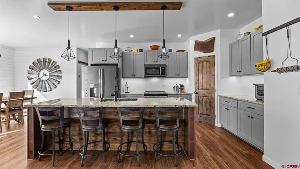 a kitchen with stainless steel appliances a stove top oven a refrigerator a dining table and chairs with wooden floor