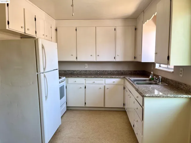 a kitchen with granite countertop a white refrigerator stove a sink and white cabinets