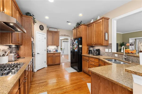 a kitchen with stainless steel appliances granite countertop a refrigerator a sink dishwasher a dining table and chairs with wooden floor